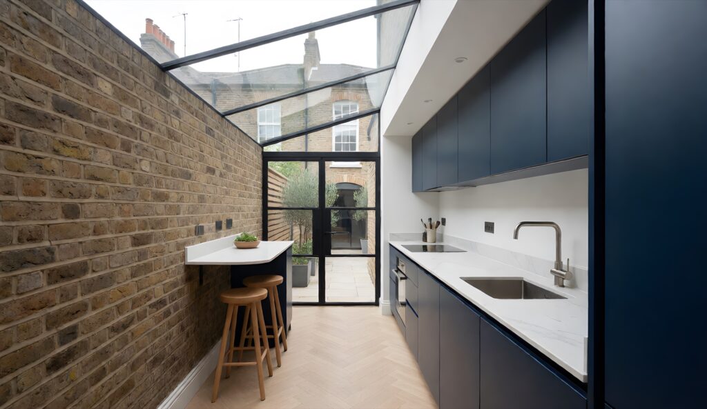 Side-return kitchen extension in a Victorian terrace with a glass roof, navy cabinets and exposed brick